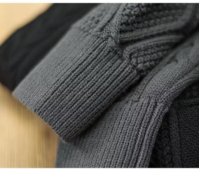 Close-up of a dark gray knitted sweater with a textured pattern on a beige surface.