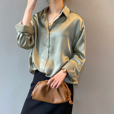 Person wearing a light green satin shirt holding a brown handbag against a plain background