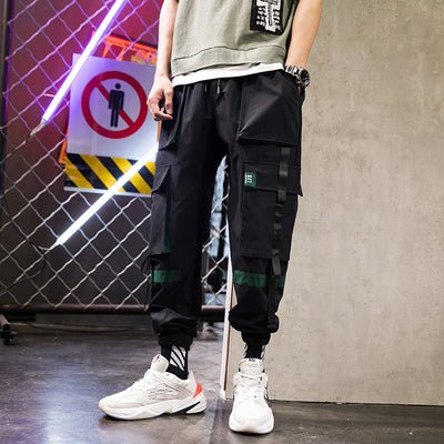 Person wearing black cargo pants with green accents and white sneakers in an urban setting.