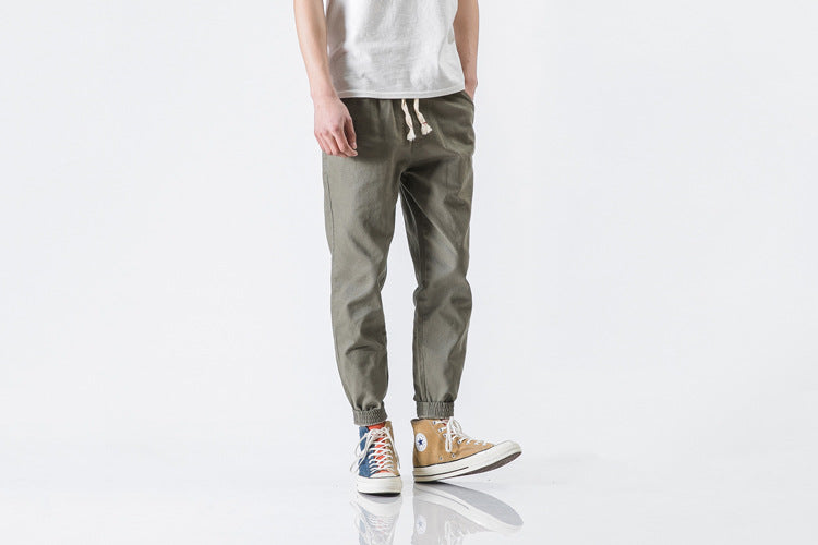 Person wearing olive green jogger pants and brown shoes on a white background