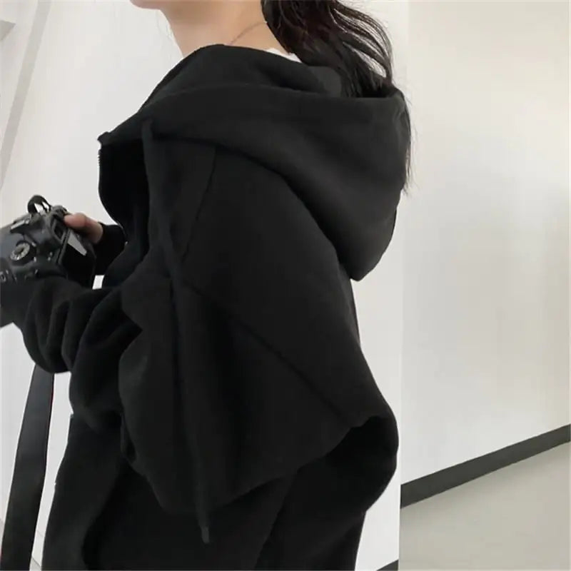 Person wearing a black hoodie holding a camera against a white background