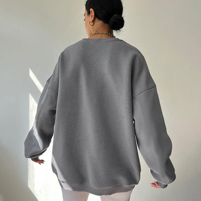 Person wearing a gray oversized sweater standing in a softly lit room.