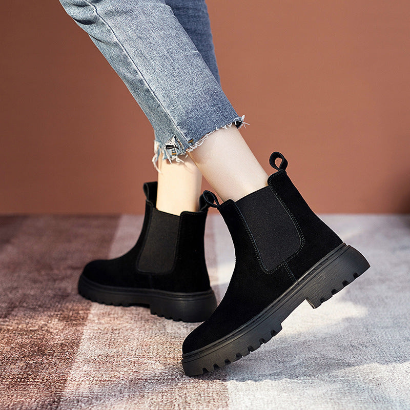 Black Chelsea boots worn with light blue jeans on a checkered floor.