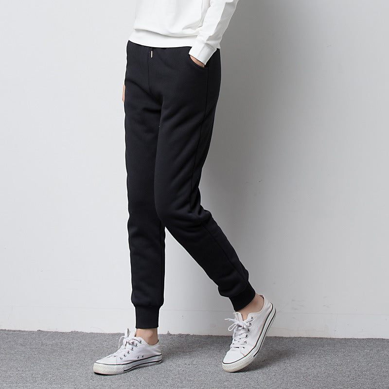 Person wearing black fleece jogger pants for women and white sneakers on a plain background