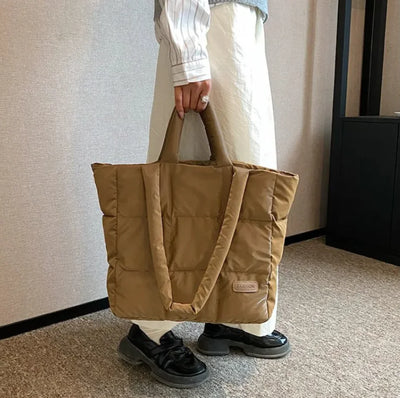 Person holding a brown quilted tote bag indoors.