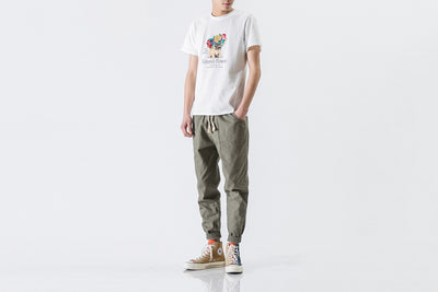 Person wearing a white t-shirt with colorful graphics and green pants on a white background