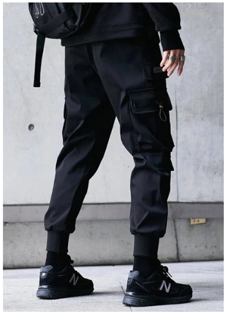 Person wearing black cargo pants and black sneakers against a concrete wall.
