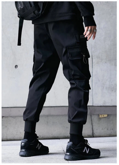 Person wearing black cargo pants and black sneakers against a concrete wall.