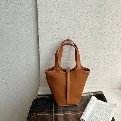 Brown leather tote bag on a textured surface with a light gray background