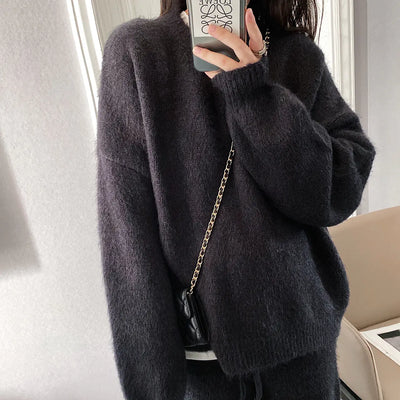 Person wearing a dark gray sweater with a gold chain bag, standing indoors.
