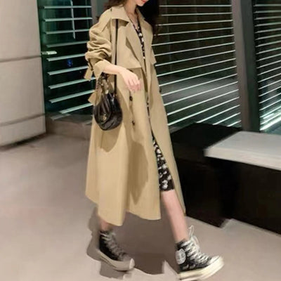 Person wearing a beige trench coat with black sneakers indoors.