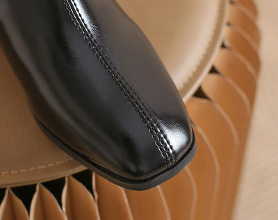 Close-up of a black leather shoe with a beige background