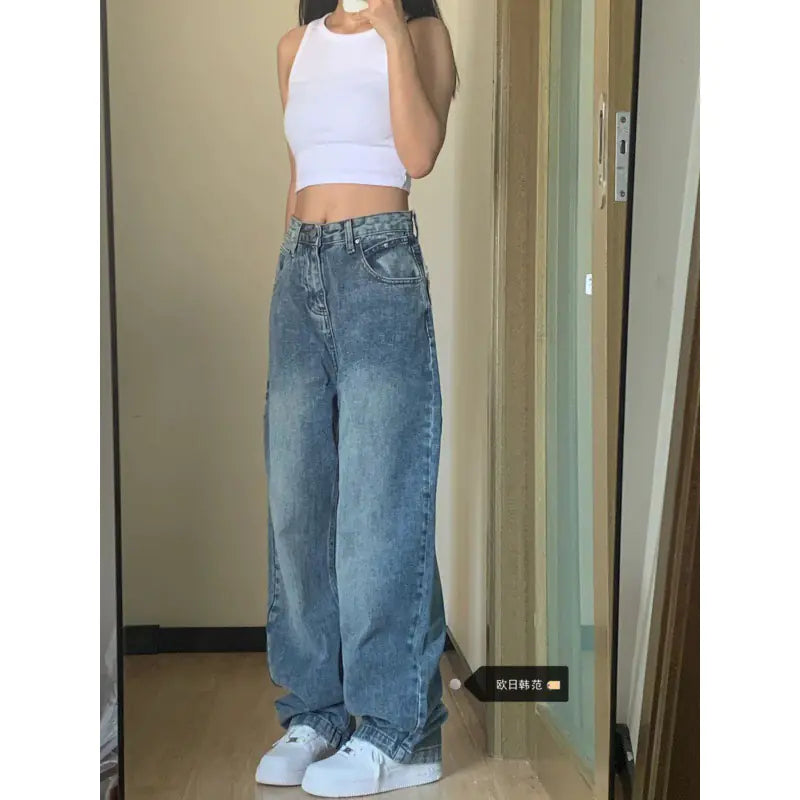 Person wearing a white crop top and blue jeans standing in front of a mirror.