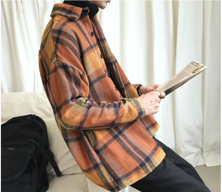 Person wearing a plaid jacket holding a book against a white curtain background