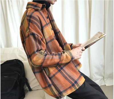 Person wearing a plaid jacket holding a book against a white curtain background