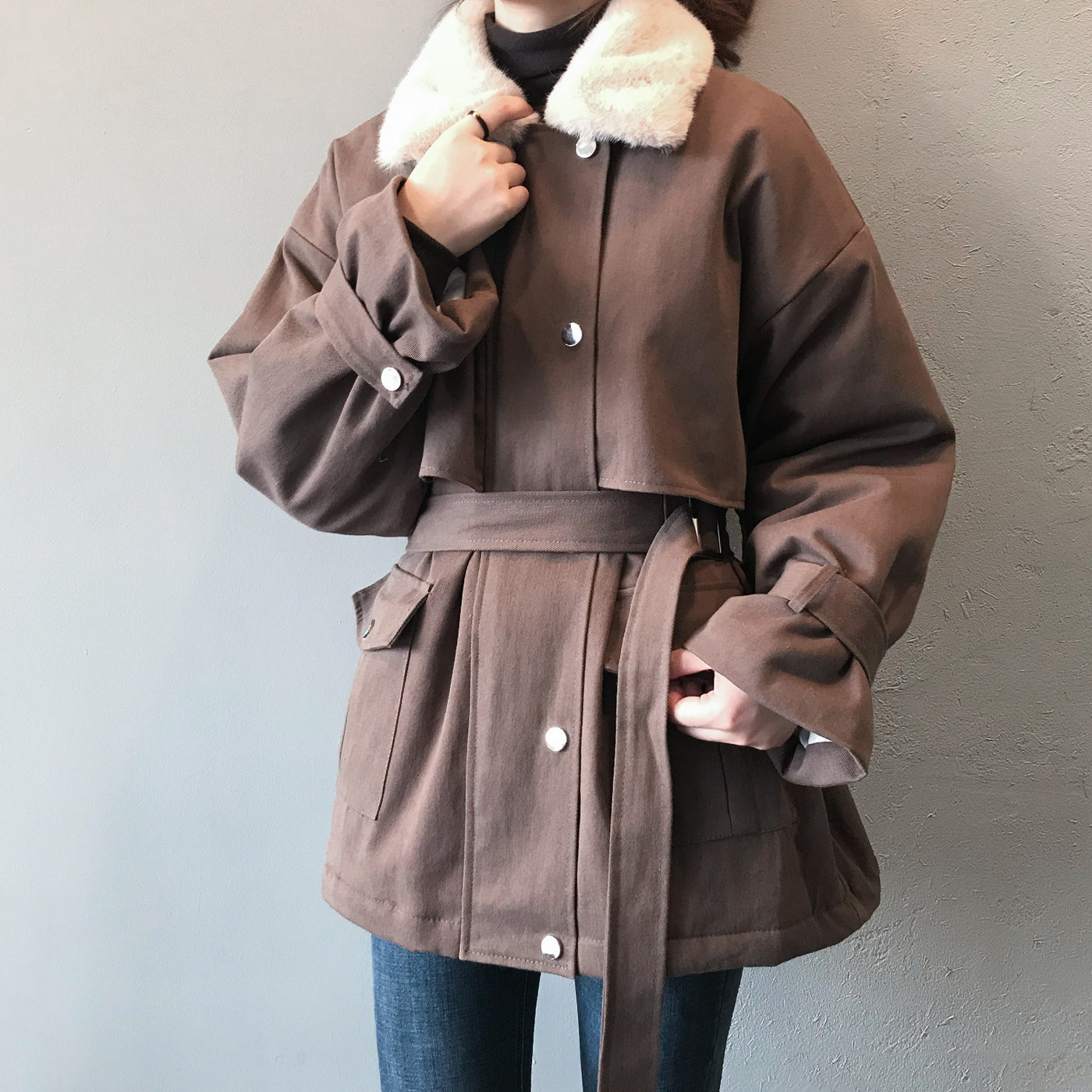 Brown coat with white fur collar worn by a person against a gray background