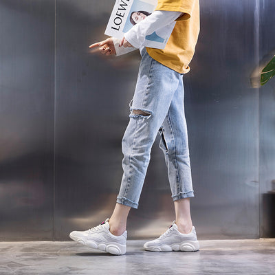 Person wearing light blue ripped jeans and white sneakers, holding a magazine with a blurred background.