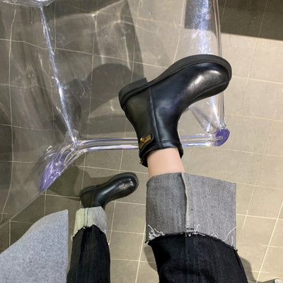 Person wearing black boots with a visible brand logo on a tiled floor.