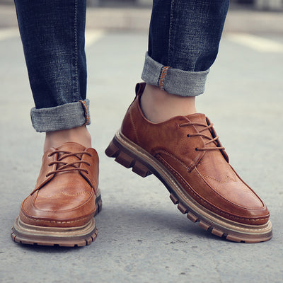 Brown leather shoes worn with rolled-up jeans on a blurred background