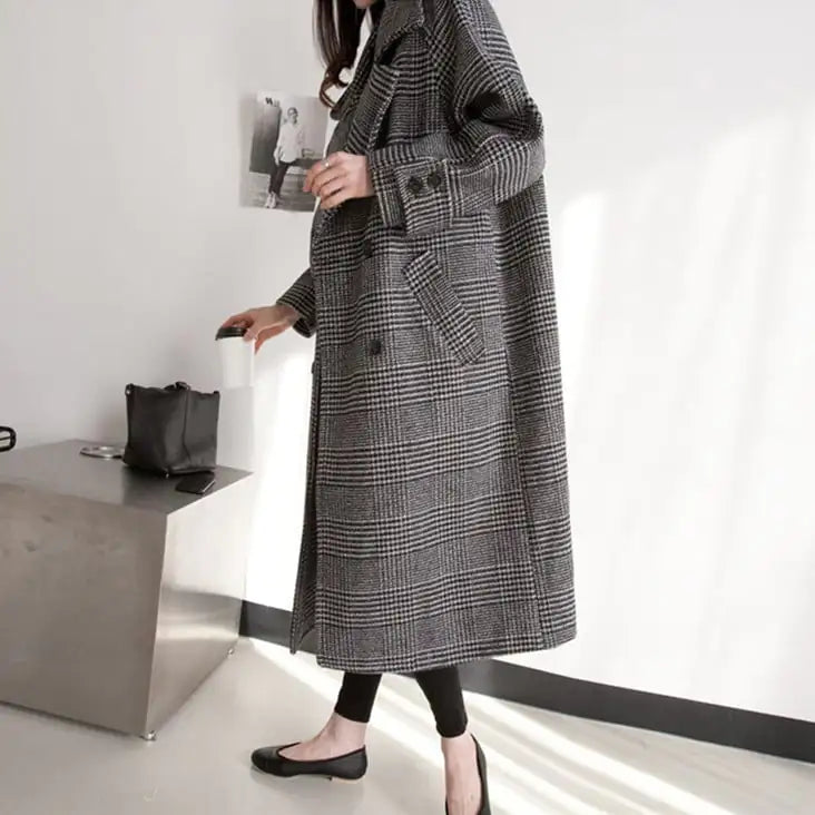 Person wearing a long gray checkered coat in a minimalistic setting