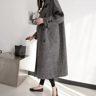 Person wearing a long gray checkered coat in a minimalistic setting