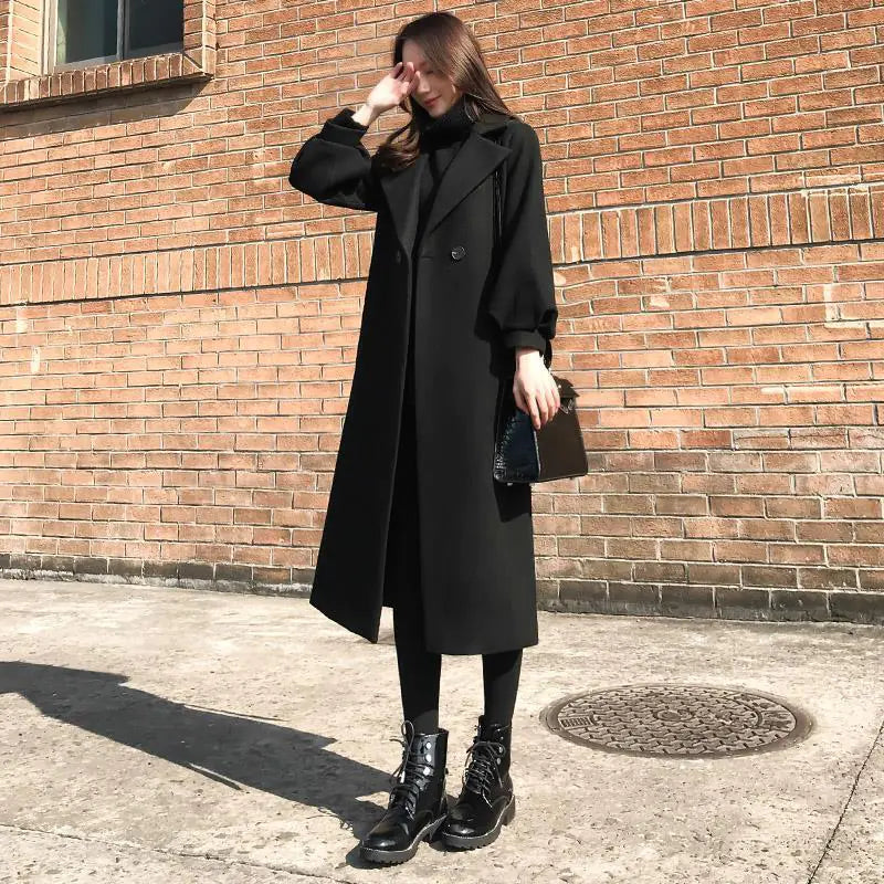 Person wearing a black coat standing against a brick wall.