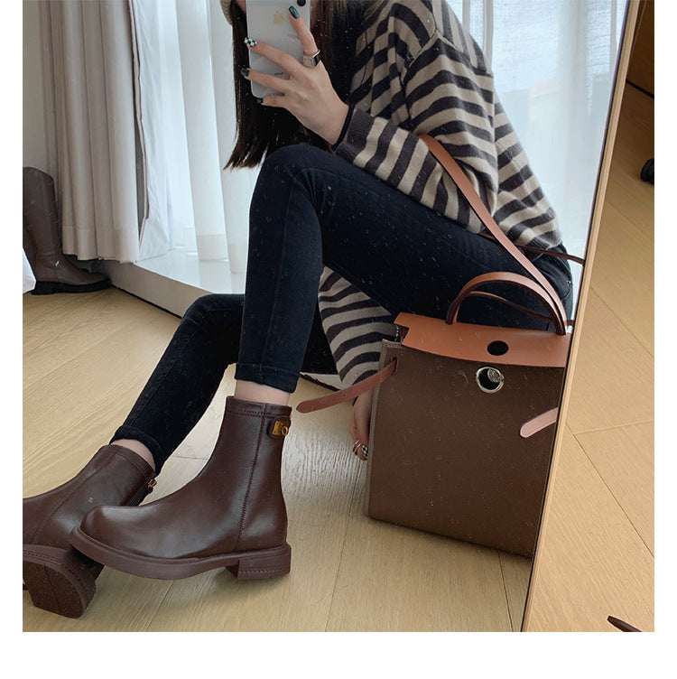 Person wearing brown ankle boots sitting on a wooden floor with a brown handbag.
