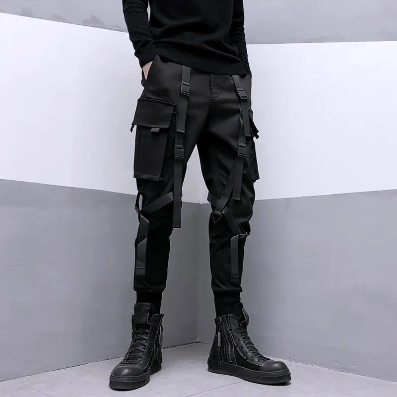 Person wearing black cargo pants and black boots against a gray and white background