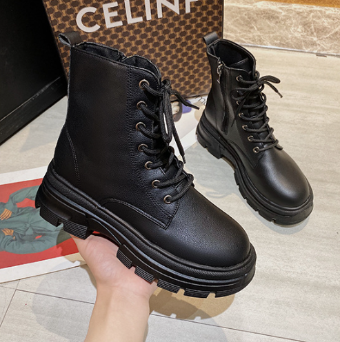Black leather boots held by a hand with a patterned box in the background