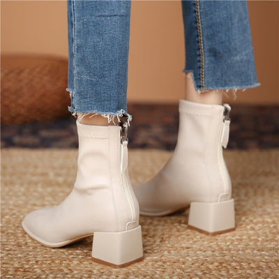 White ankle boots with block heels worn with blue jeans on a textured surface.