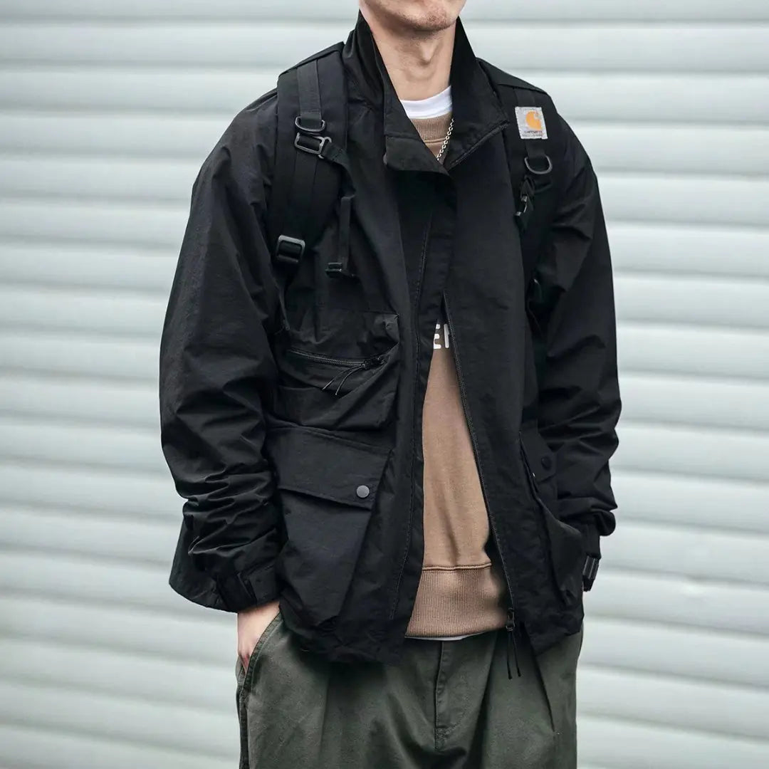 Person wearing a black jacket with a brand logo, standing against a gray background