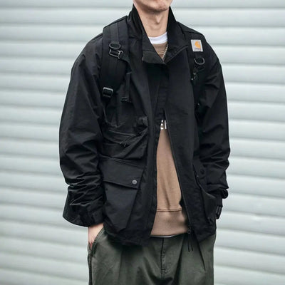 Person wearing a black jacket with a brand logo, standing against a gray background