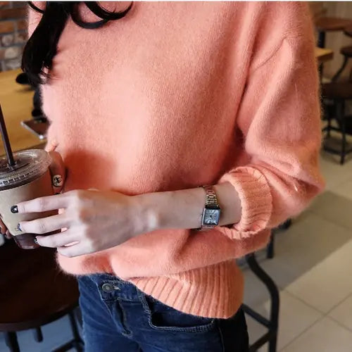 Person wearing a pink sweater holding a drink in a casual setting
