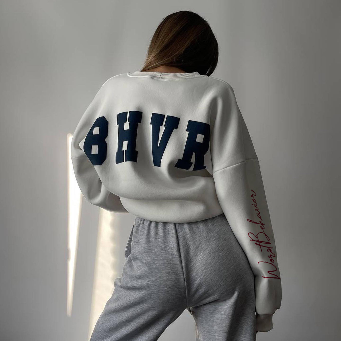 Person wearing a white sweatshirt with blue 'BHVR' branding and gray pants against a neutral background