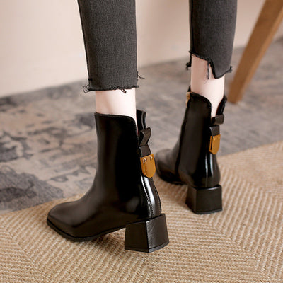 Black ankle boots with brown accents worn with black jeans on a carpeted floor.