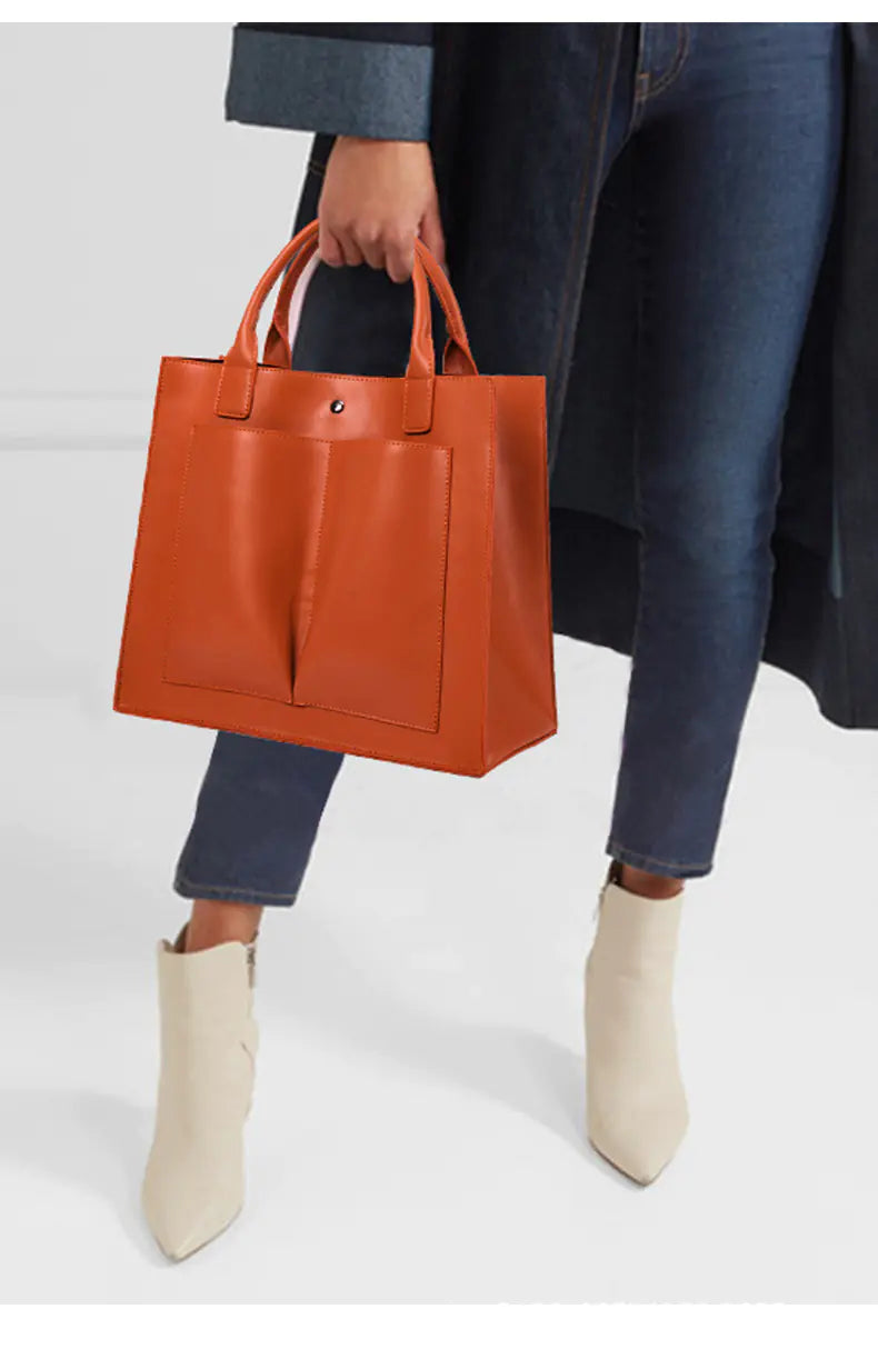 Person holding an orange leather tote bag on a white background