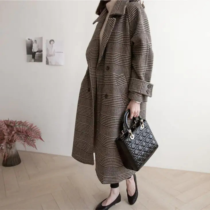 Person wearing a long plaid coat holding a black handbag indoors.