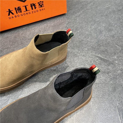 Brown and gray Chelsea boots with decorative buttons on a gray surface, featuring a brand box in the background.