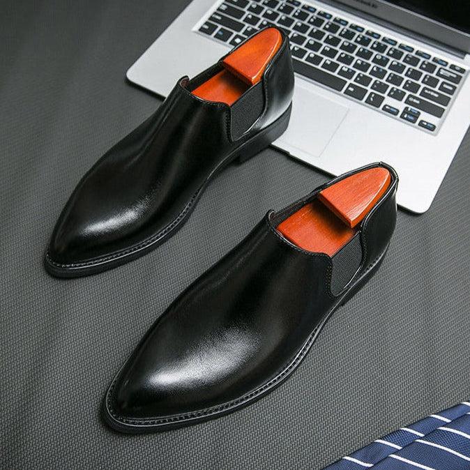 Black dress shoes with orange lining on a gray surface next to a laptop.