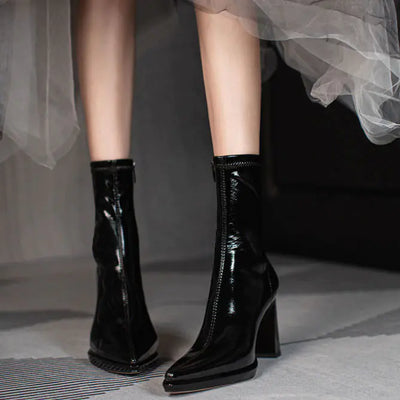 Black patent leather ankle boots worn with a white skirt on a neutral background