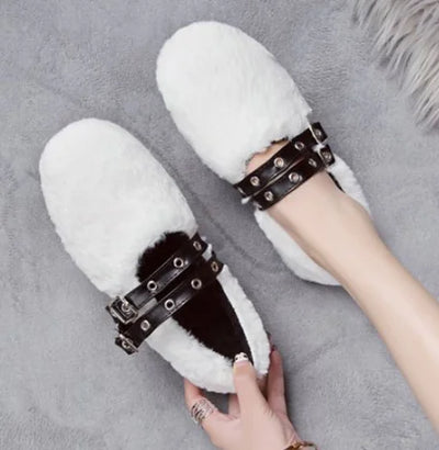 White fluffy slippers with black straps held by a hand on a gray surface