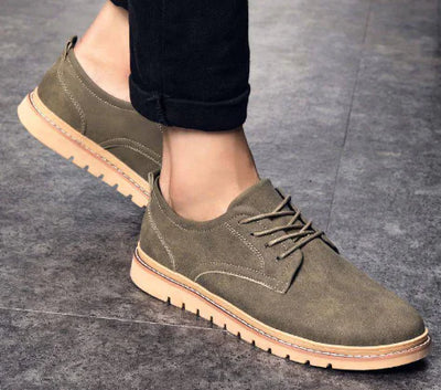 Green suede shoes with brown soles worn by a person on a gray floor.
