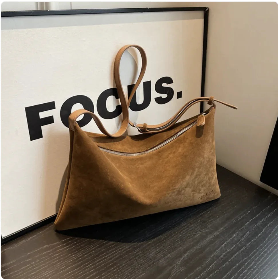 Brown handbag on a wooden surface with a 'FOCUS' poster in the background