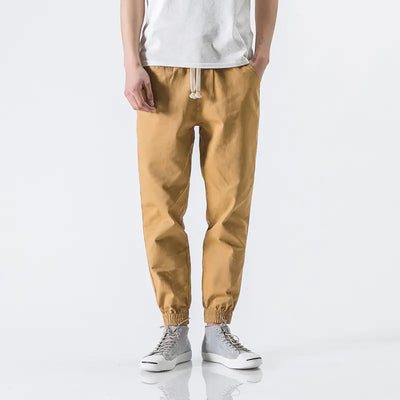Person wearing mustard yellow jogger pants and white sneakers on a white background