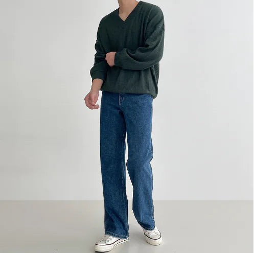 Person wearing a green sweater and blue jeans on a plain background