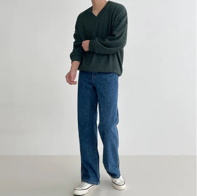 Person wearing a green sweater and blue jeans on a plain background