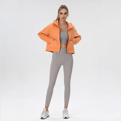 Woman wearing an orange jacket and gray leggings on a white background