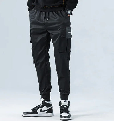 Person wearing black cargo pants and black sneakers with white soles on a light gray background