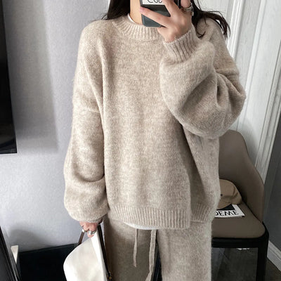 Person wearing a beige sweater and pants in a room with a chair and table.
