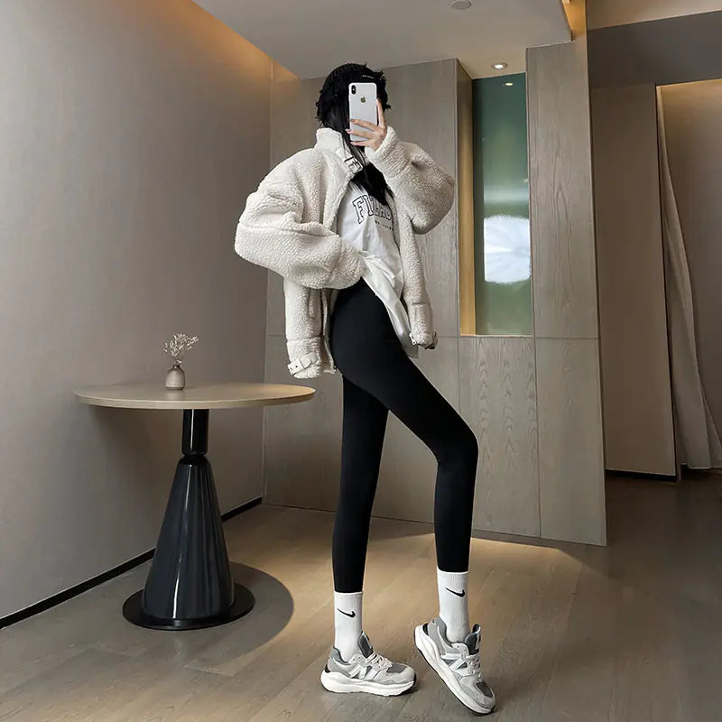 Person wearing a white fluffy coat, black leggings, and white sneakers in a modern interior setting.